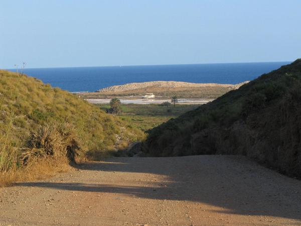 Meerblick auf dem Weg zum Strand
Nachdem der Steinweg auf eine Hügelkette führt, erblickt man zum erstenmal das Meer. Davor eine Meersalzanlage.