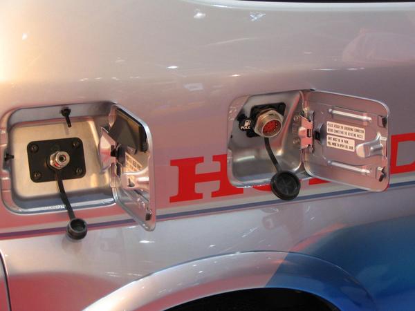 Honda FCX hydrogen rezervor
Mai inainte de a deschide capacul din stanga pentru incarcarea cu gas a rezervorului, trebuie facuta impamantarea, legarea la masa, a capacului din dreapta.
