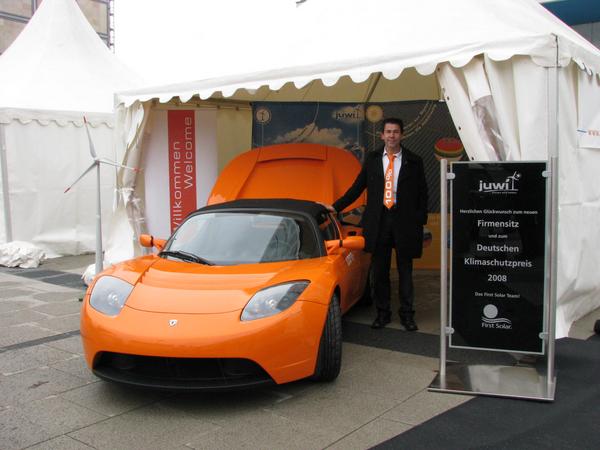 Tesla first owner in Germany
Juwi-founder and corporate governance Matthias Willenbacher with the first in Europe for public roads certified Tesla. Right a CdTe Cadmium Tellurit photovoltaic from First Solar.